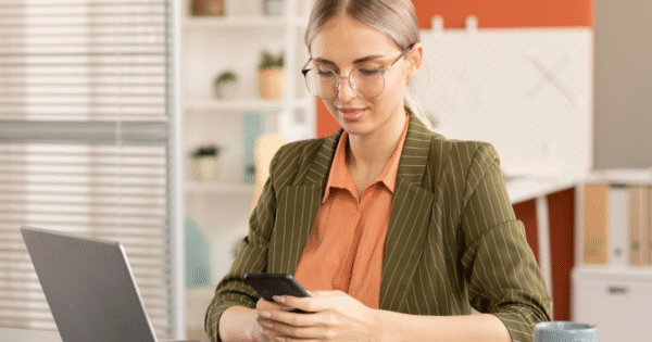 Mujer joven revisando el móvil en su escritorio mientras trabaja en marketing digital y redes sociales.